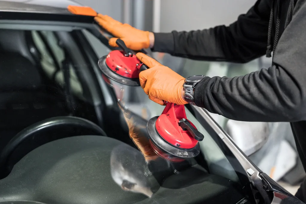 Close-up of a worker in orange gloves using red suction cup handles to replace a car windshield.